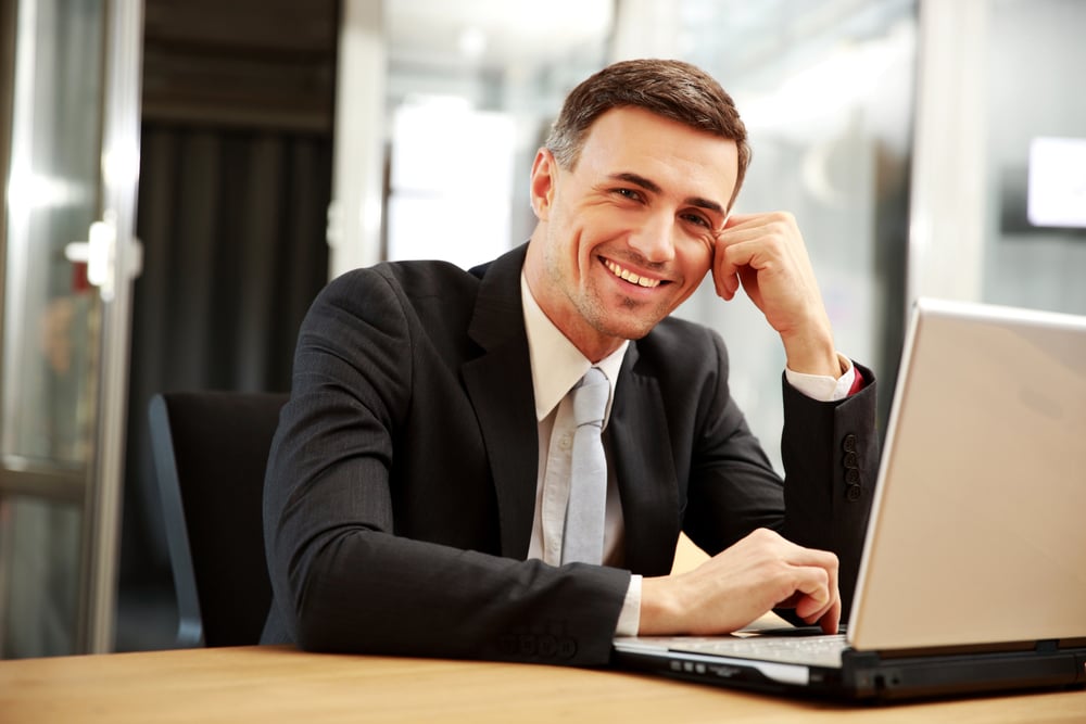 Smiling businessman sitting with laptop at office