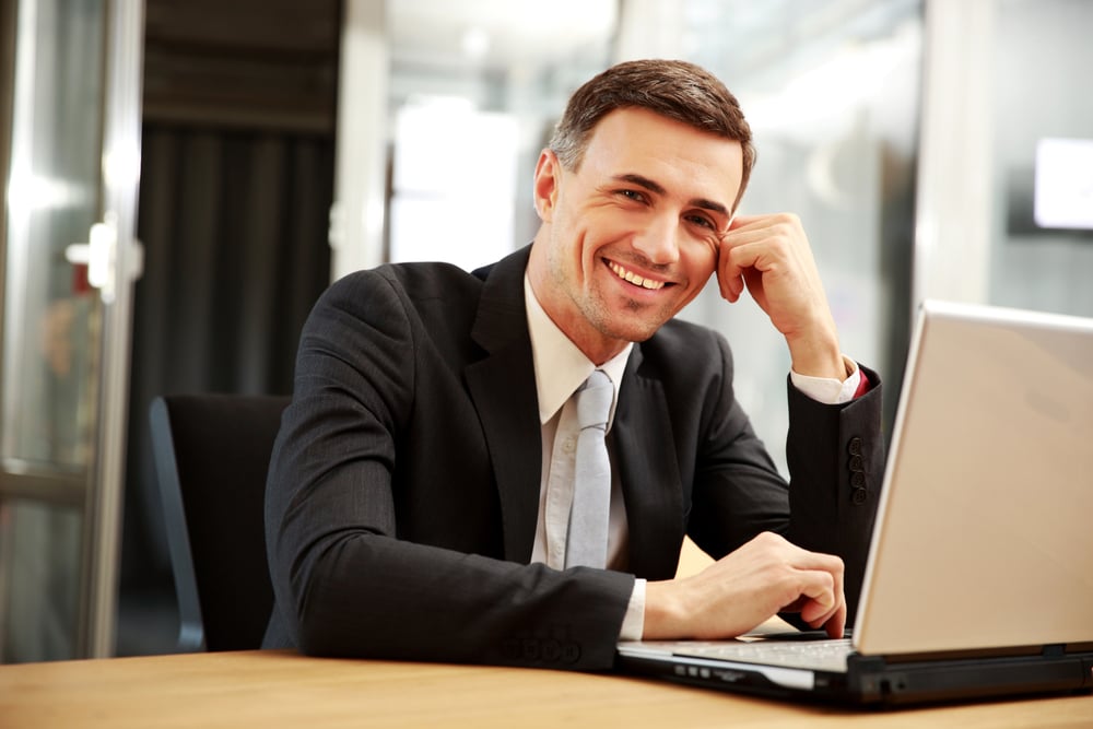 Smiling businessman sitting with laptop at office Smiling businessman sitting with laptop at office